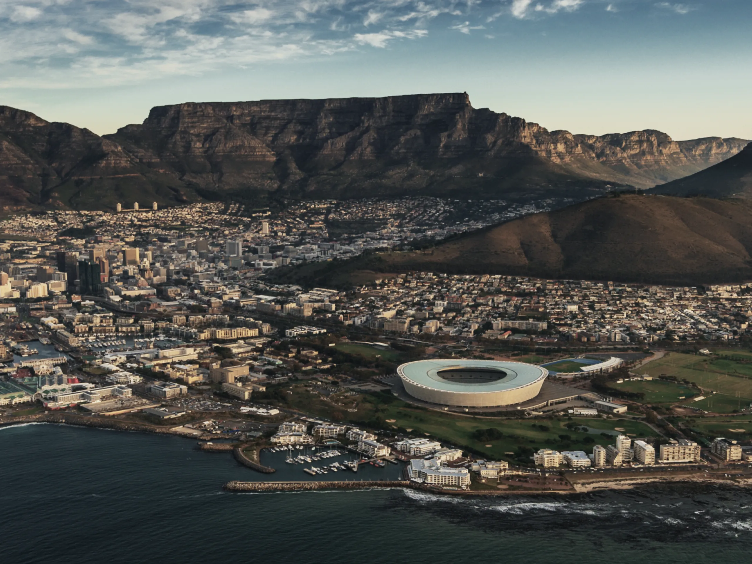 Aerial view of Cape Town, South Africa, featuring the Cape Town Stadium and Table Mountain in the background.