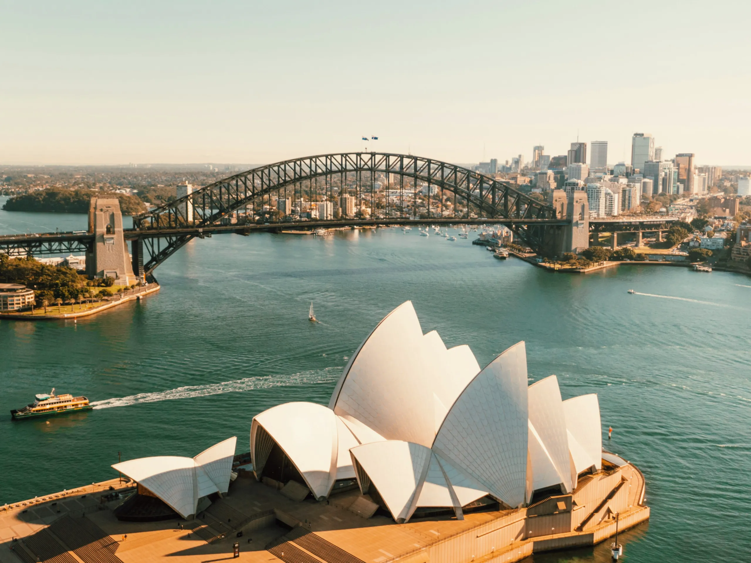 Aerial view of the Sydney Opera House on the harbor with the Sydney Harbour Bridge in the background.
