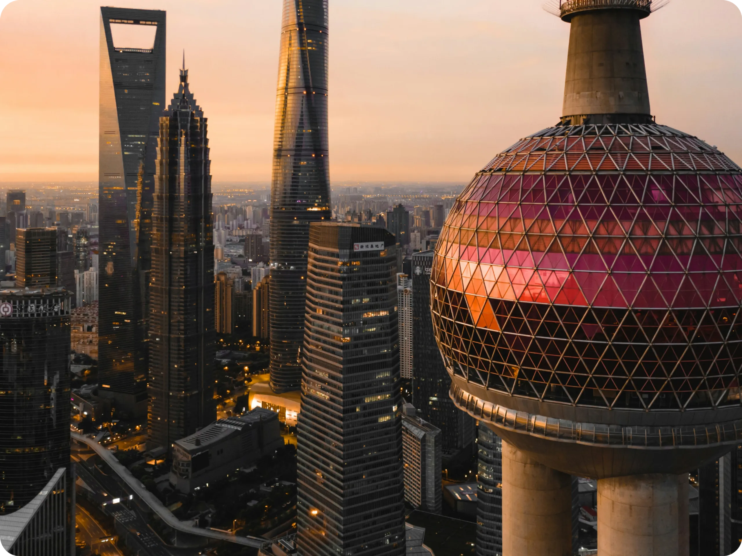 Shanghai skyline at sunset, featuring the Oriental Pearl Tower with its distinctive pink spheres and nearby modern skyscrapers, including the Shanghai World Financial Center and Shanghai Tower. City lights begin to illuminate.
