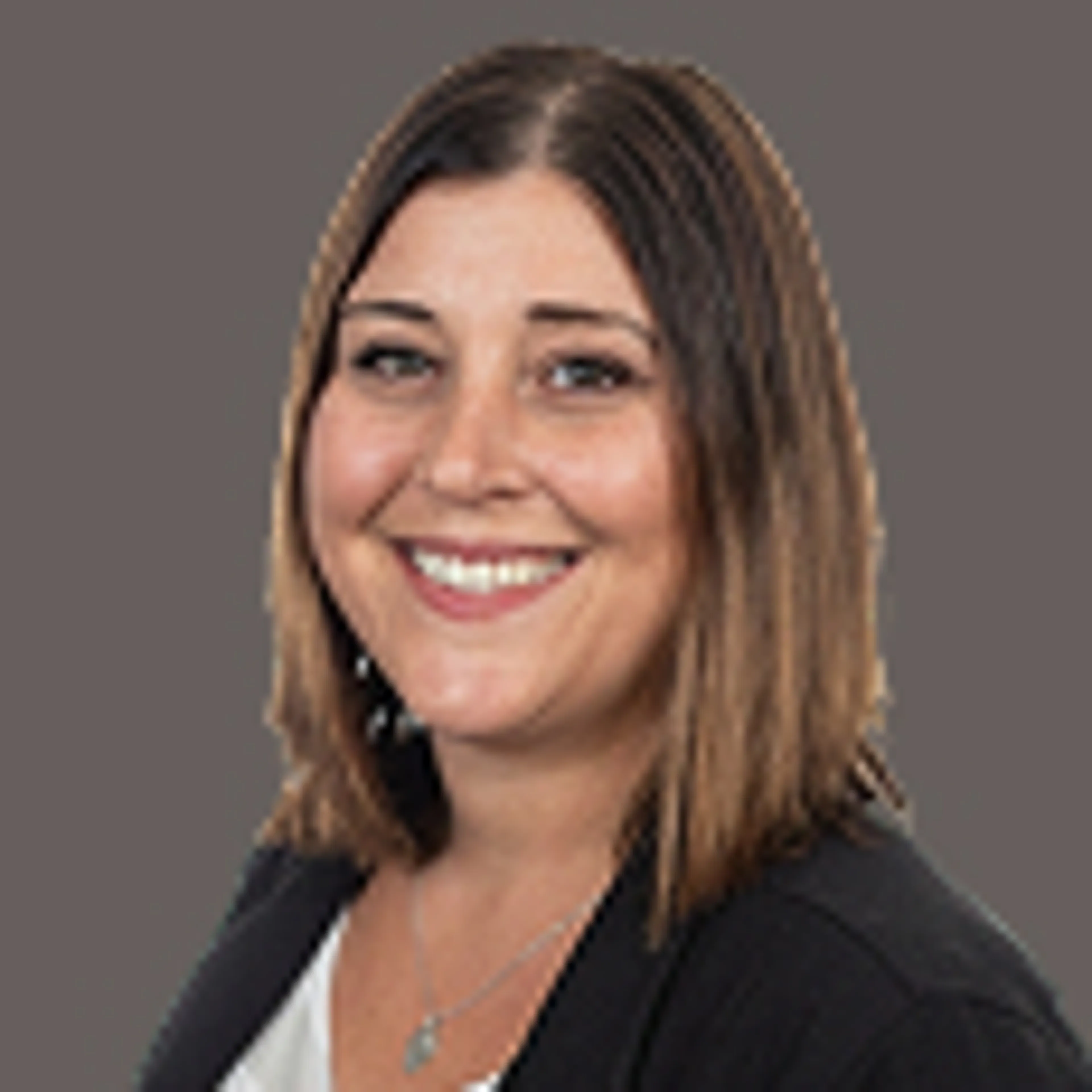 Smiling woman with straight, shoulder-length brown hair, wearing a black blazer over a light top, posed in front of a plain gray background.