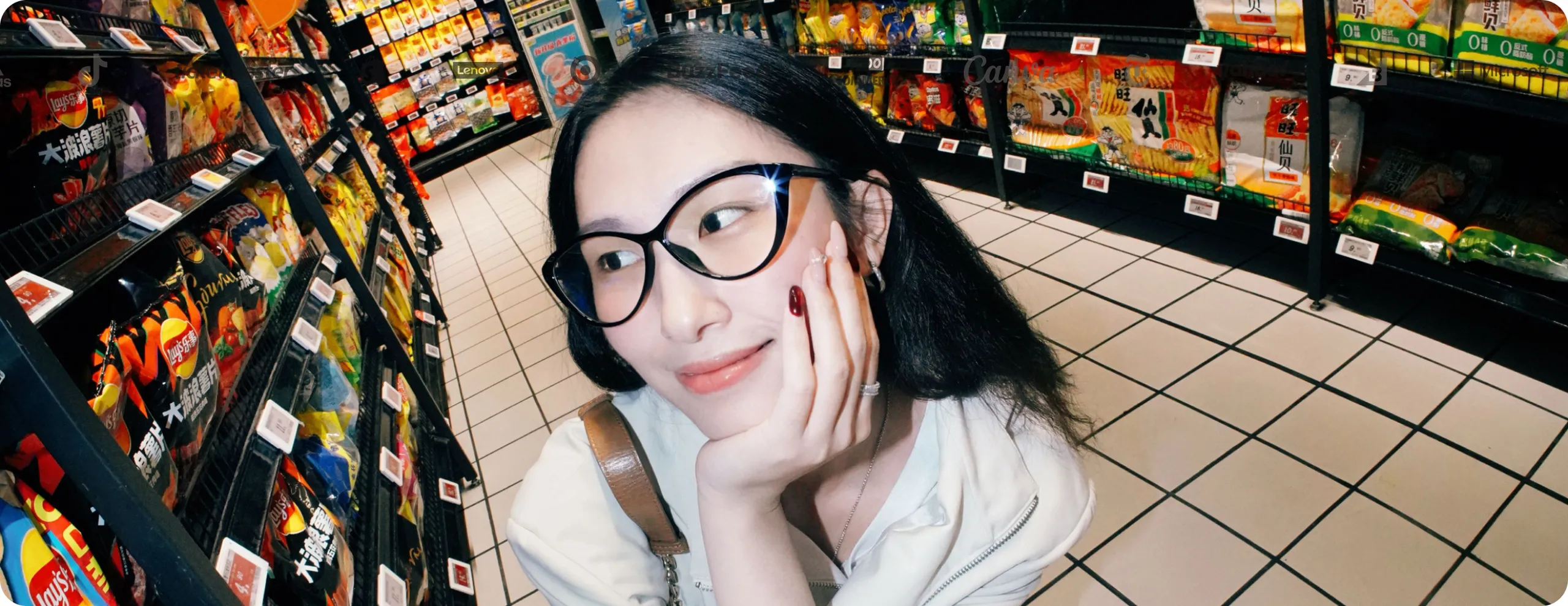 A person with glasses smiles while standing in an aisle of a grocery store, surrounded by colorful snacks on the shelves.