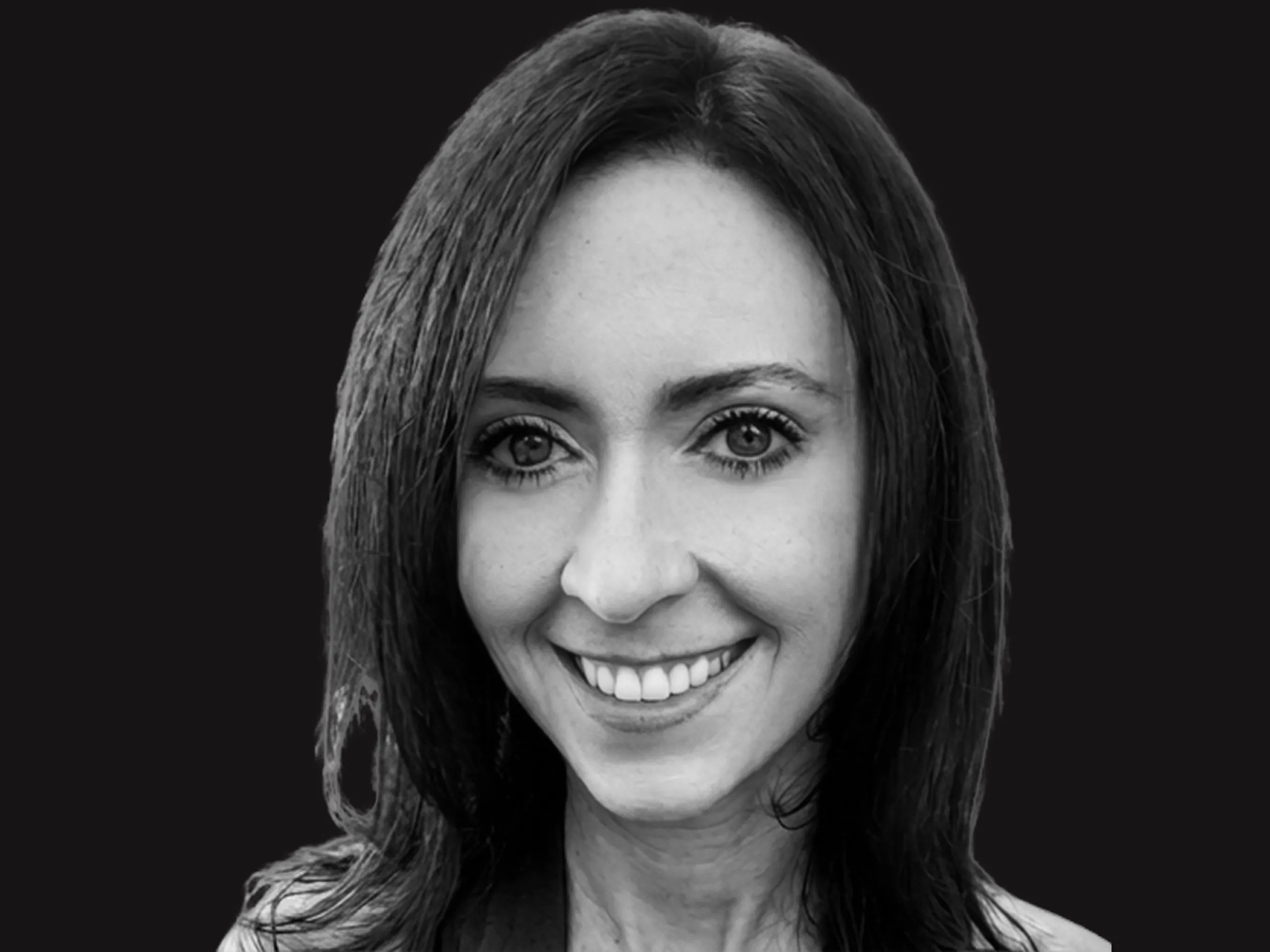 Smiling woman with straight, dark hair looks at the camera in a black and white portrait with a plain black background.