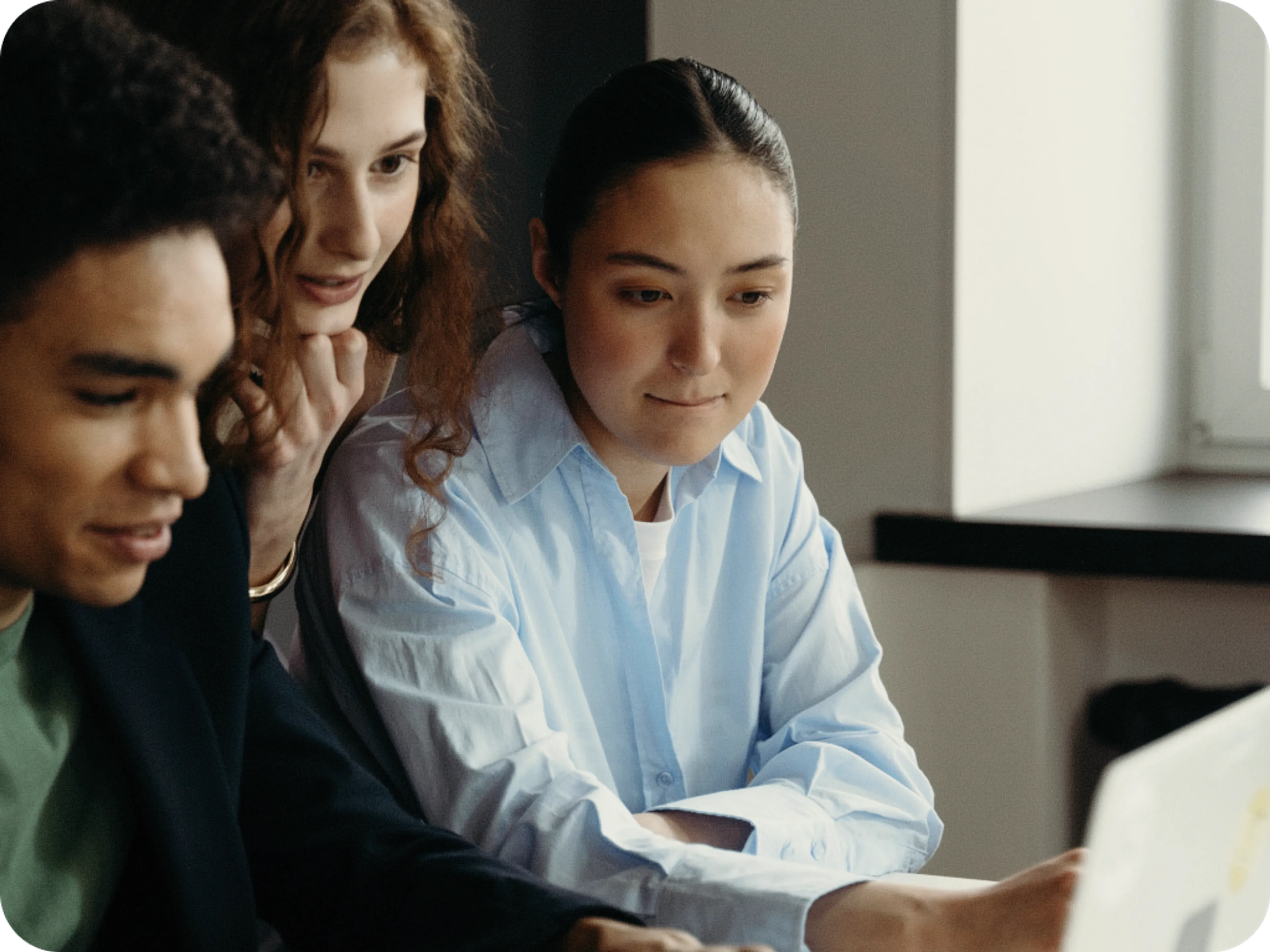 Three people looking at a laptop screen together.