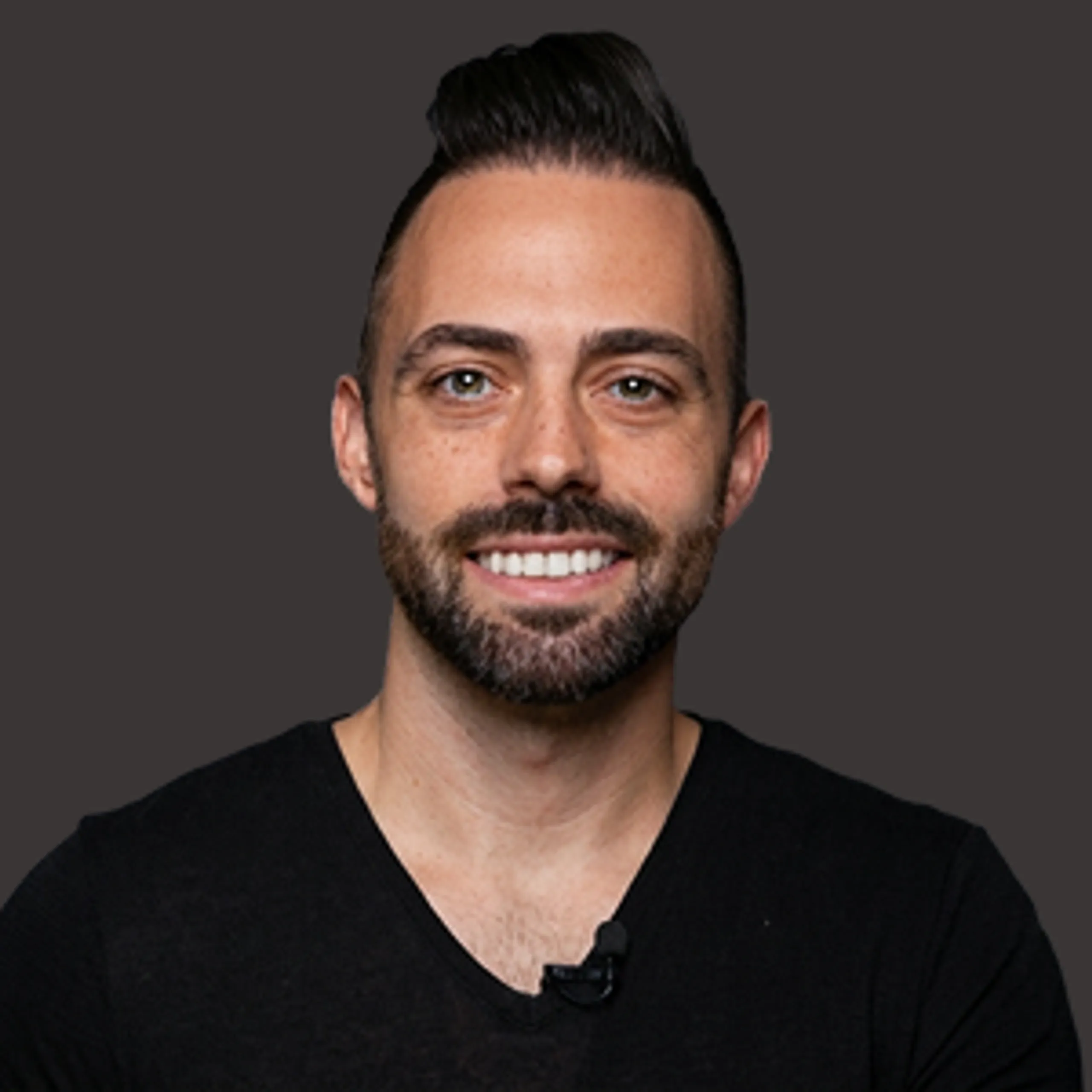 Smiling man with short dark hair and beard, wearing a black shirt, posed against a plain dark background.