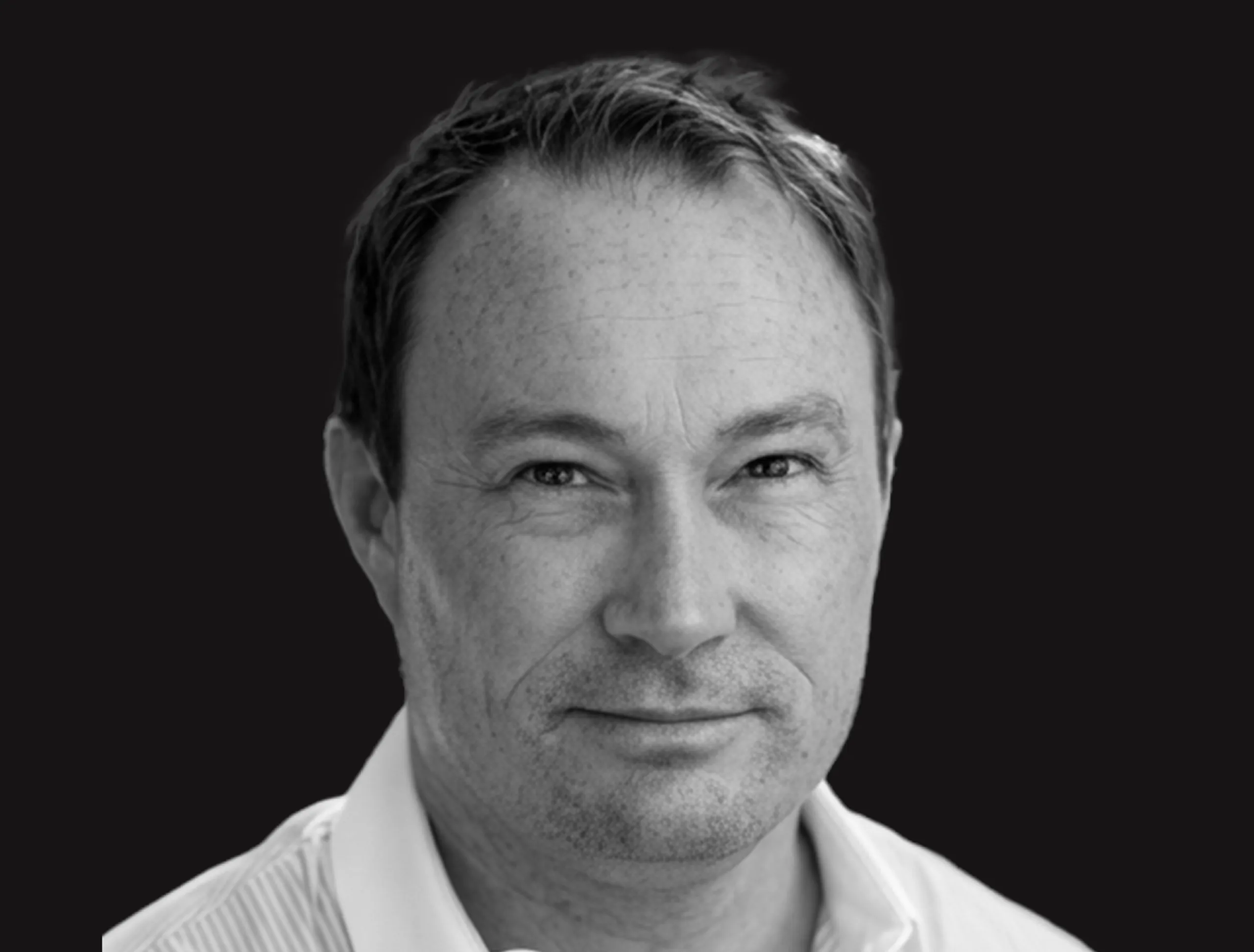 Black-and-white portrait of a middle-aged man with short hair, wearing a collared shirt, facing the camera with a neutral expression against a dark background.
