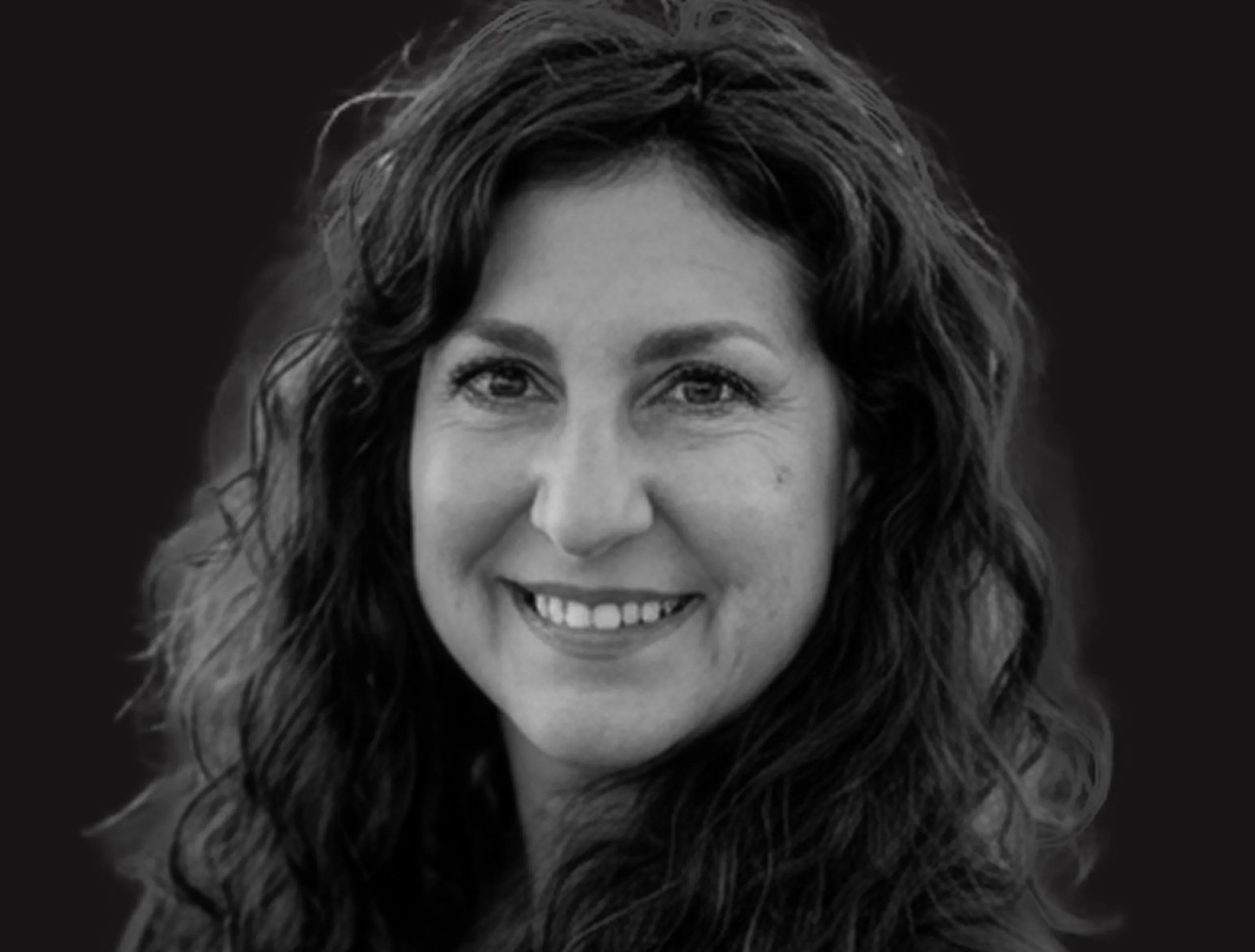 Smiling woman with long, wavy dark hair, shown in a black and white portrait against a plain dark background.