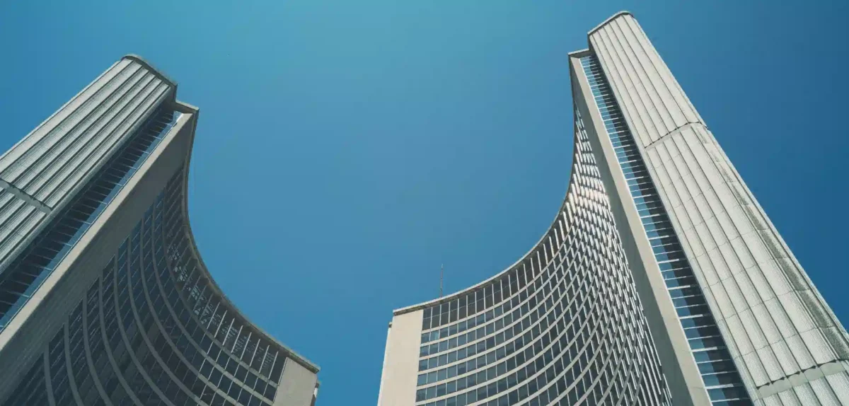 Two modern skyscrapers curve upward against a clear blue sky, showcasing a blend of glass and concrete architecture.