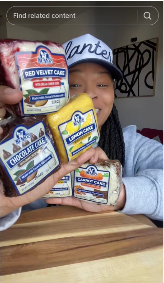 A person holds four different cake boxes: Red Velvet, Chocolate, Lemon, and Carrot, showcasing delicious dessert options.