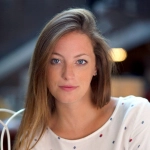 A woman named Hannah Kirschner with blue eyes is seated at a table, engaged in a thoughtful moment.