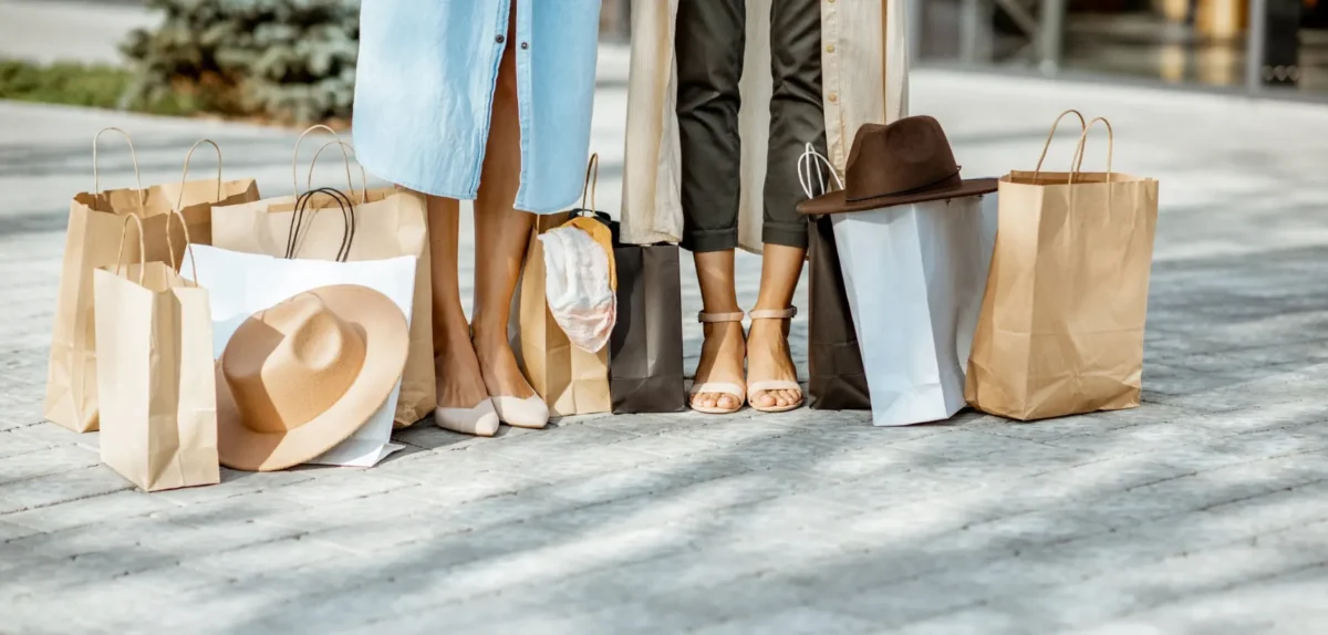 Two women stand with shopping bags in hand, appearing cheerful and engaged in conversation during their shopping trip.