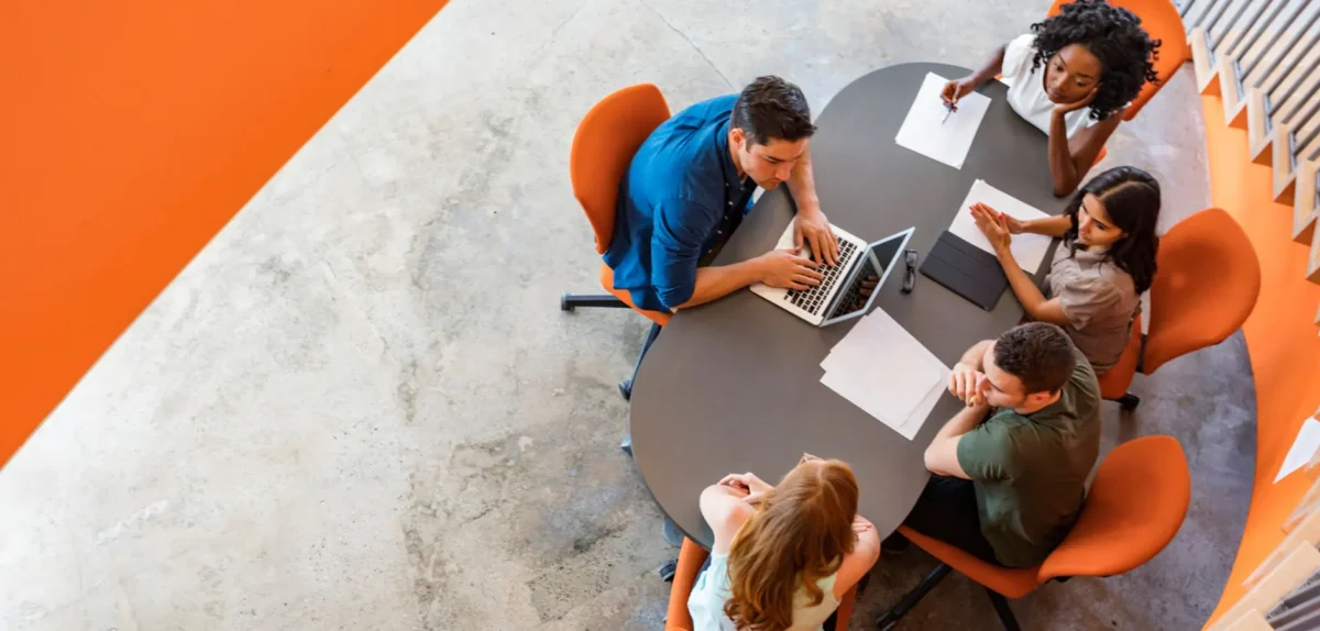 A diverse group of individuals collaborating around a table, each engaged with their laptops in a productive environment.