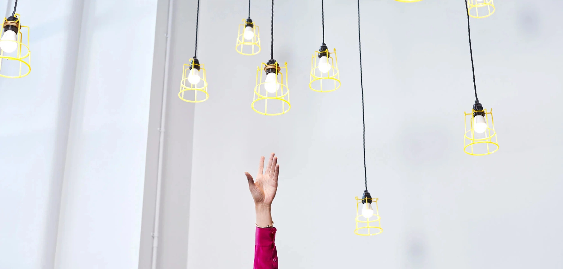 A woman stretches upward to hang light bulbs, showcasing her determination and focus in a well-lit environment.