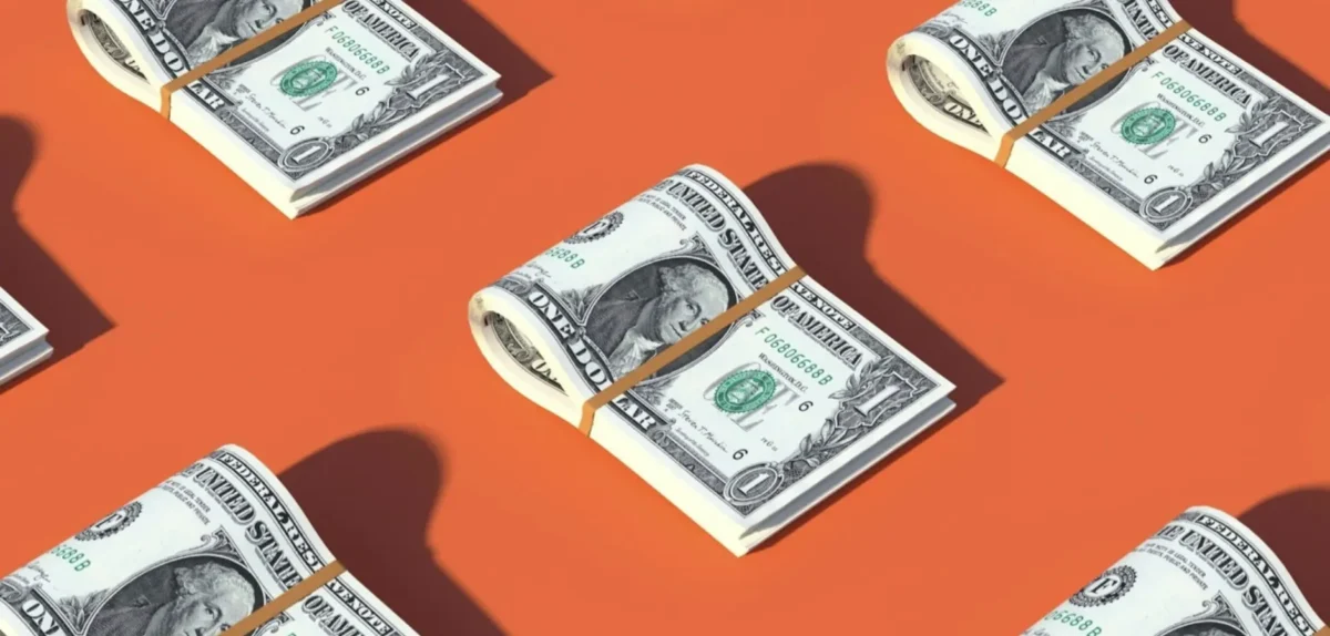 A stack of cash resting on a vibrant orange background, symbolizing wealth and prosperity.