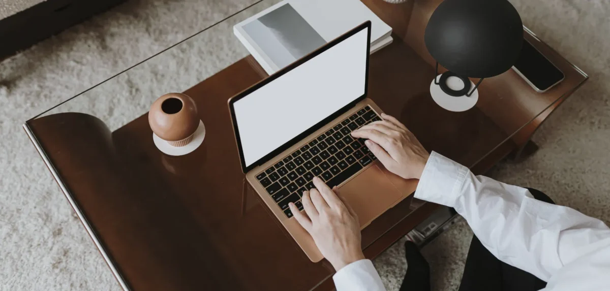 Person typing on a laptop on a wooden desk with modern decor items and a lamp.