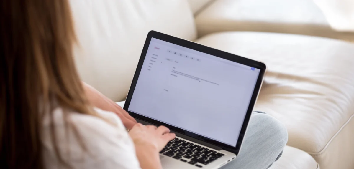 Woman using a laptop with a blurred screen on a sofa.