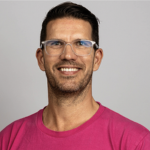 A person wearing a bright pink t-shirt poses against a light gray background, showcasing a contemporary and casual style.