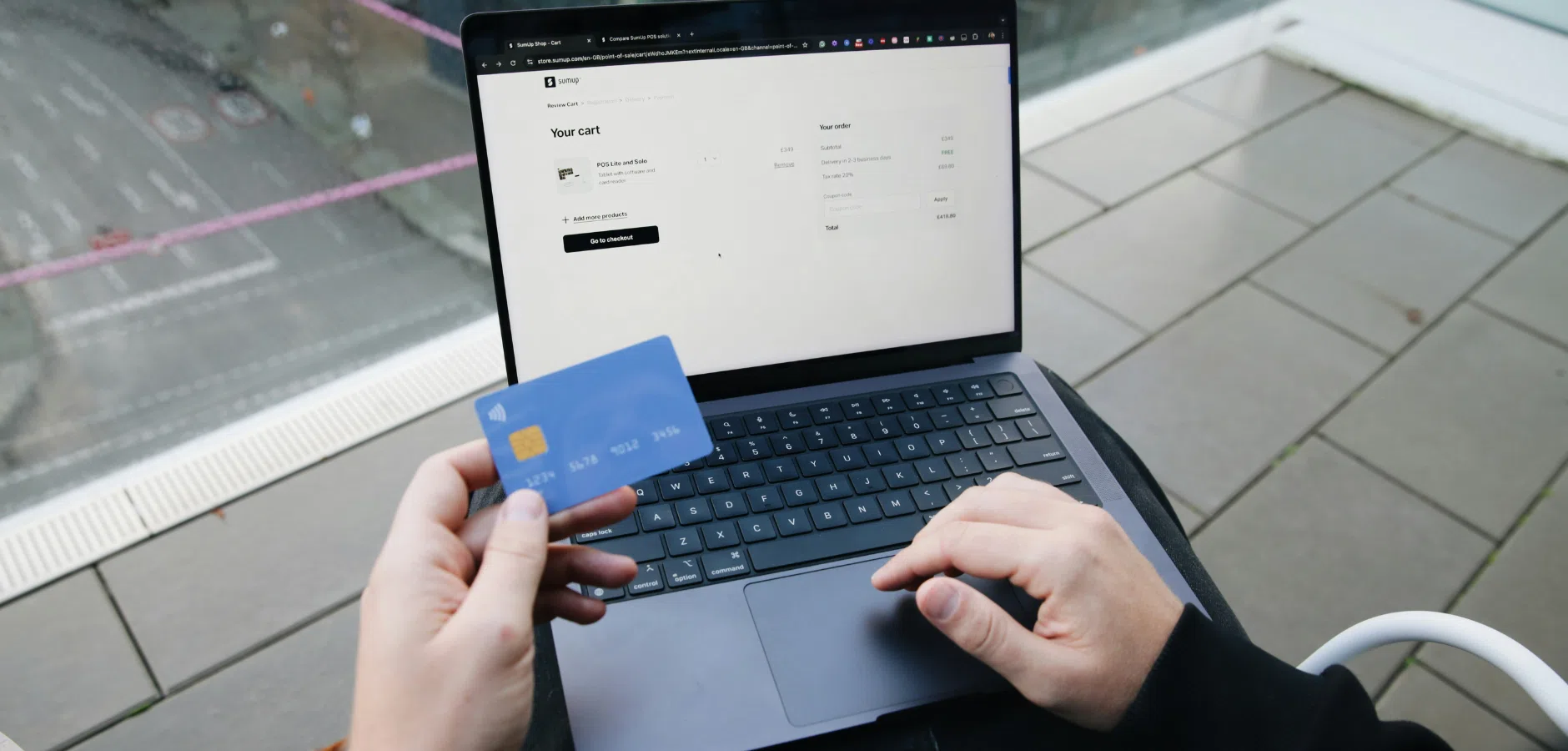 A person holds a credit card in one hand while using a laptop to review their online shopping cart.