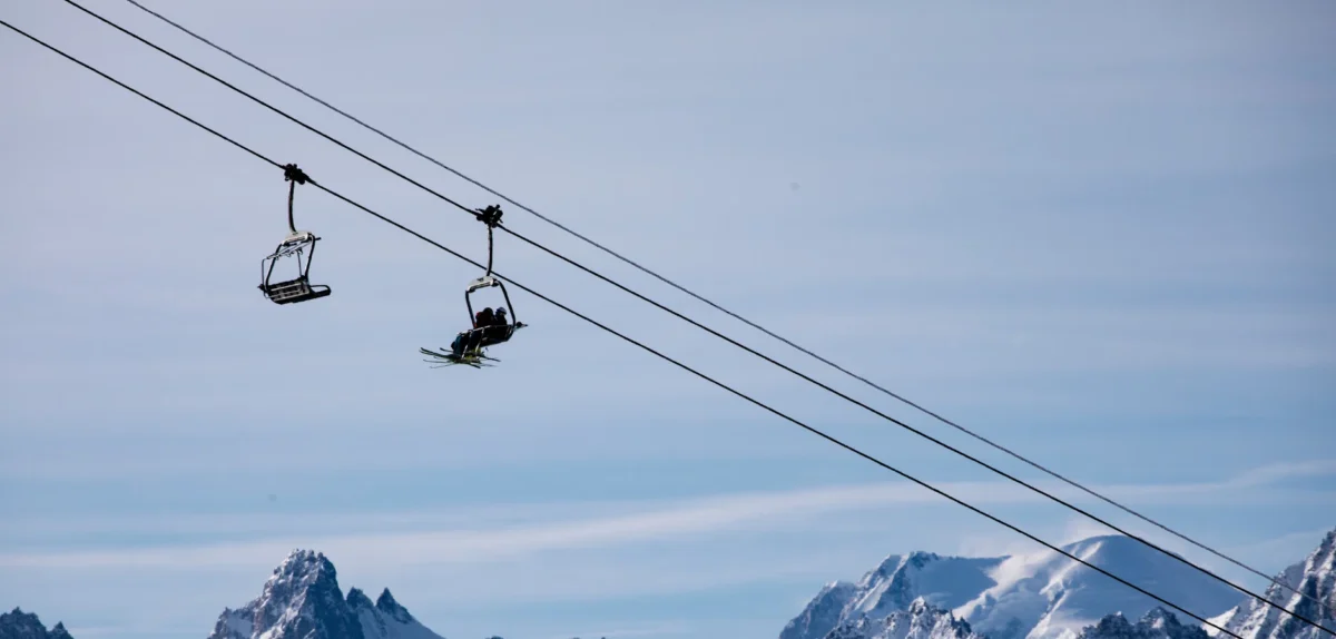 A ski lift carrying two individuals high above a snowy landscape, surrounded by winter scenery.