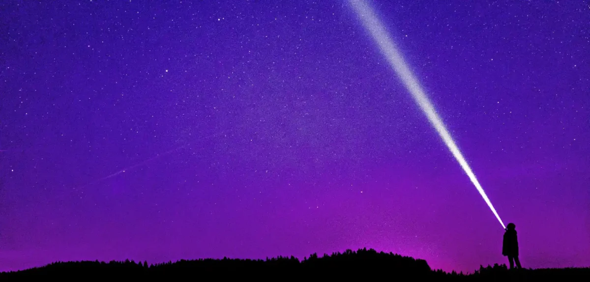 A silhouette of a person with a flashlight stands against a vibrant purple starry sky, creating a sense of wonder and exploration.