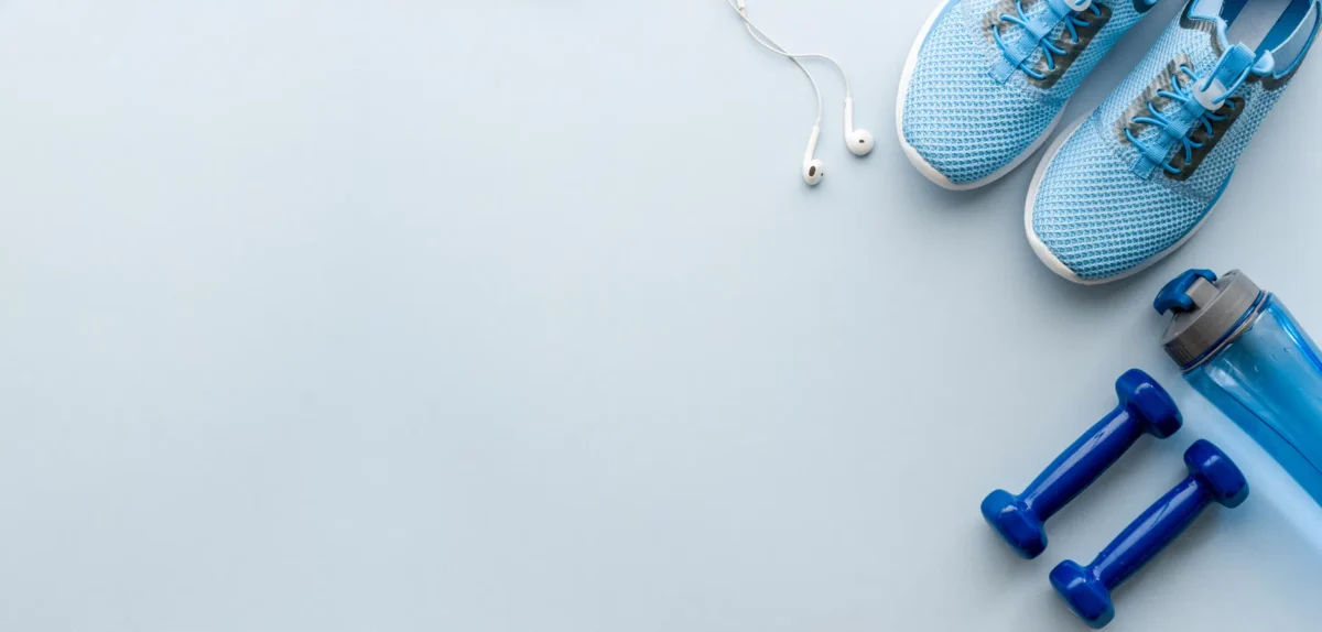 Blue athletic shoes, dumbbells, earphones, and a water bottle arranged on a light blue surface, ready for a workout.