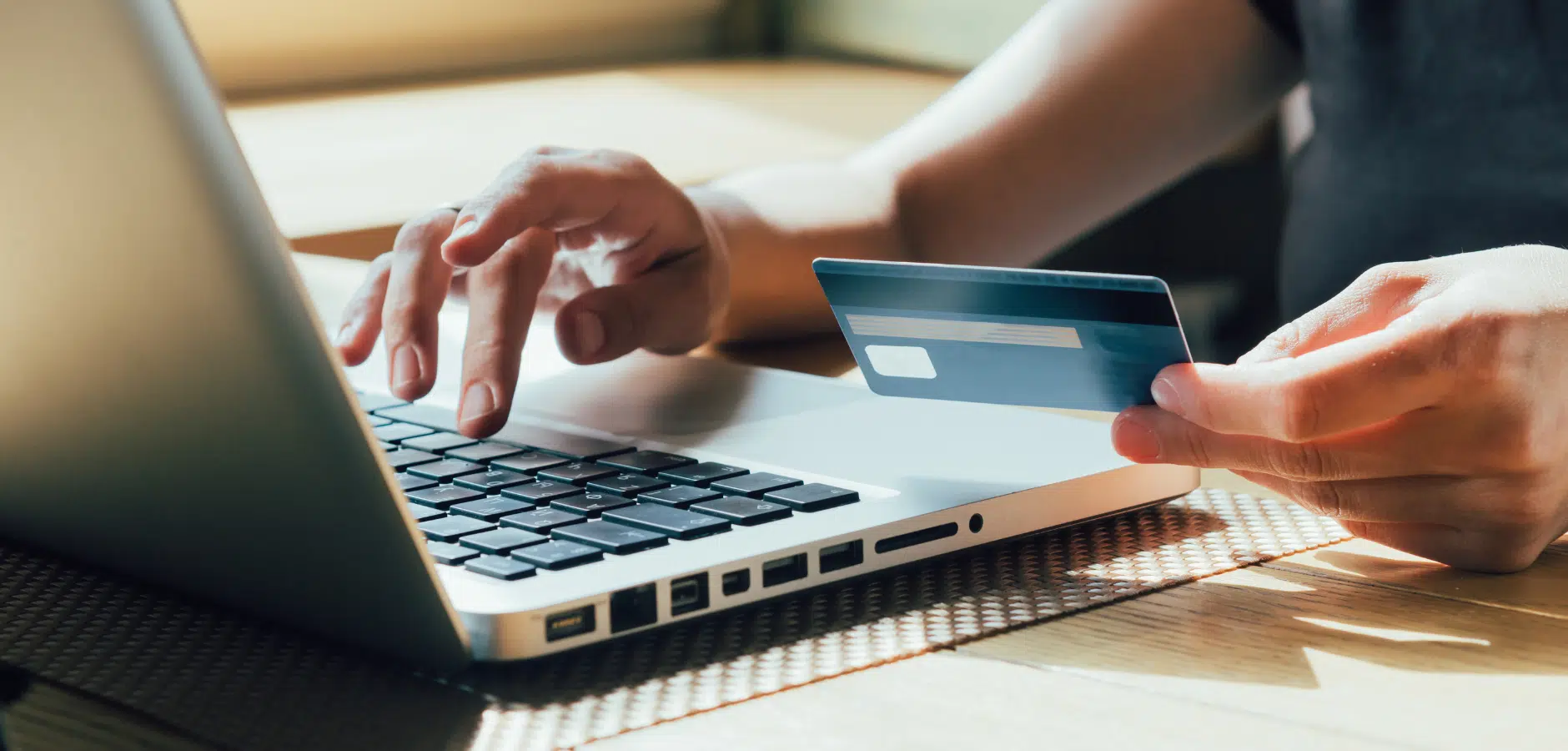 A person using a laptop to make an online purchase, holding a credit card in one hand while typing with the other.