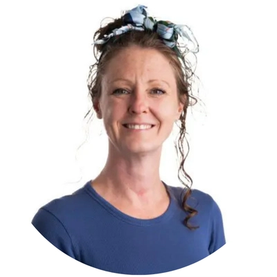 A woman with curly hair styled in a bandana, wearing a blue shirt, poses against a white background.