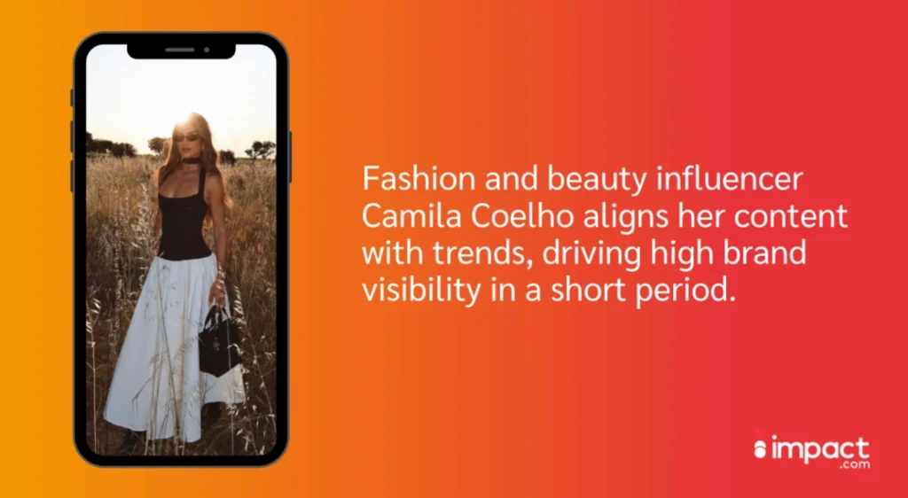 A woman in a black tank top and white skirt stands in a sunlit field, showcasing fashion trends with a stylish handbag.