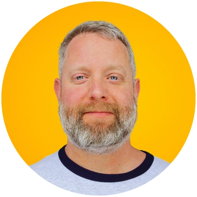 A person with short, light-colored hair and a beard is centered in a circular frame against a bright yellow background.