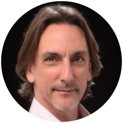 A man with long hair wearing a white shirt stands confidently, showcasing a relaxed and casual demeanor.