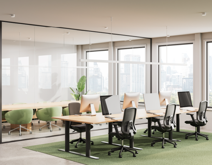 Modern office space featuring wooden desks, ergonomic chairs, and large windows with city views, enhanced by green accents.