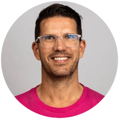 A man with short hair and glasses is wearing a bright pink T-shirt, set against a gray background in a circular crop.