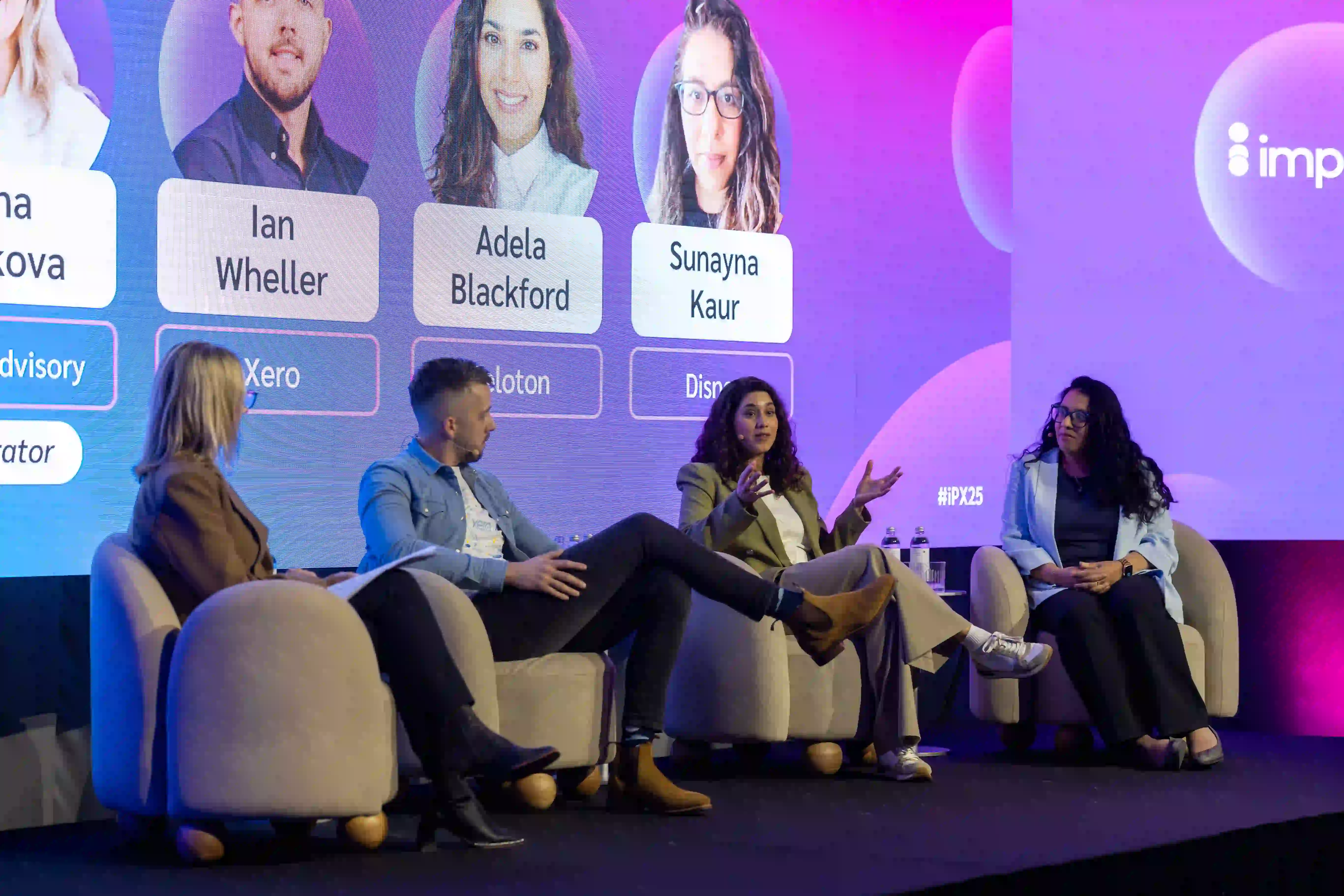 A panel discussion featuring four participants on a stage, with a colorful backdrop displaying their names and affiliations.