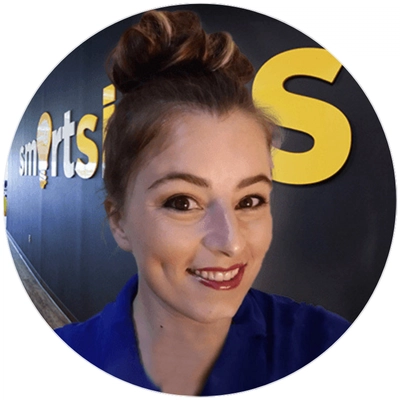 A person with a stylish bun hairstyle poses in front of a black wall with "smartsi" written in bold yellow letters.