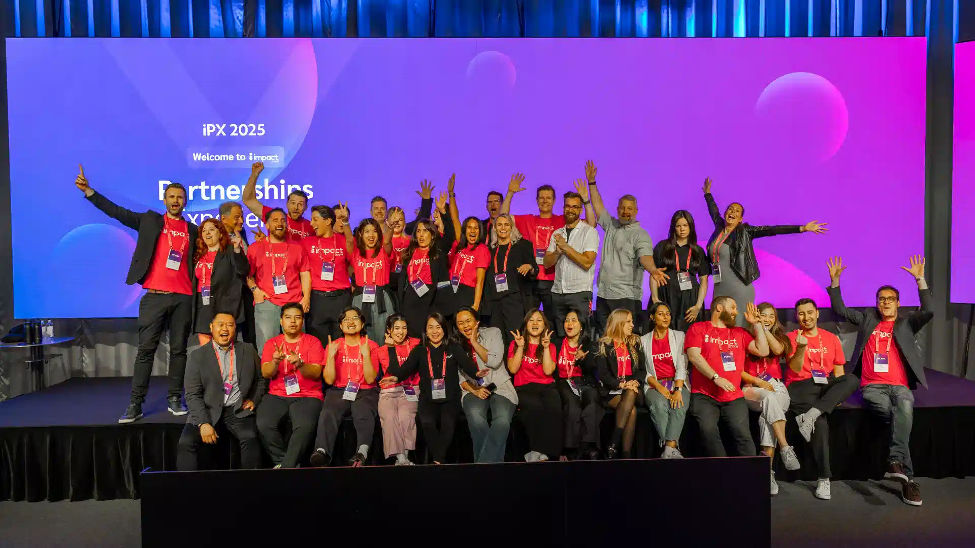 A group of people wearing red shirts stands together on stage, engaging with the audience.