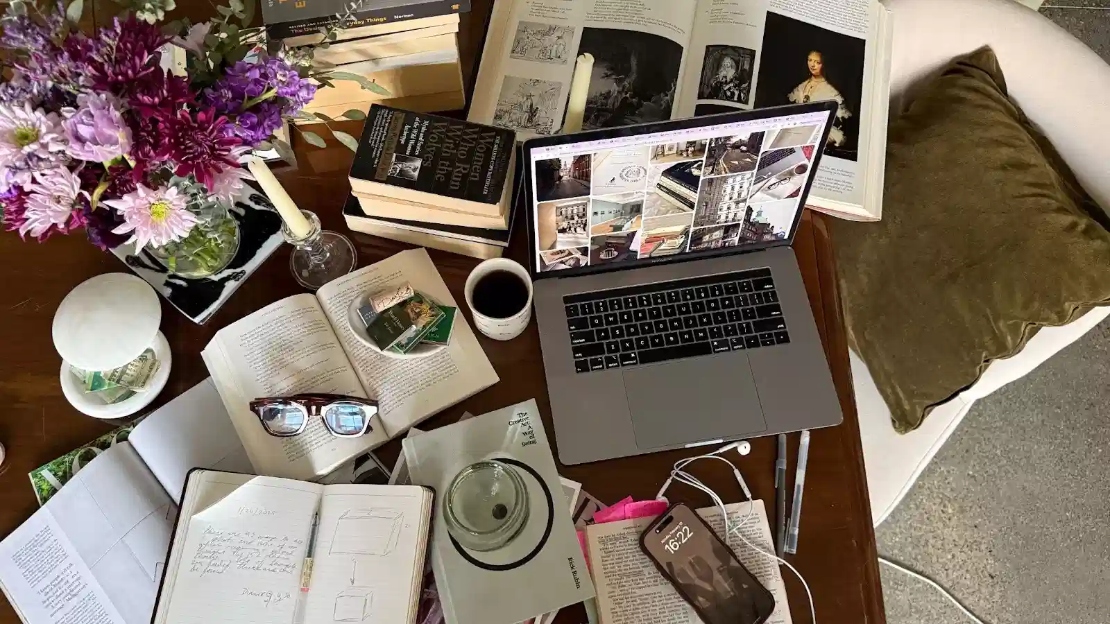 A laptop, several books, and a vase of flowers arranged neatly on a wooden table.