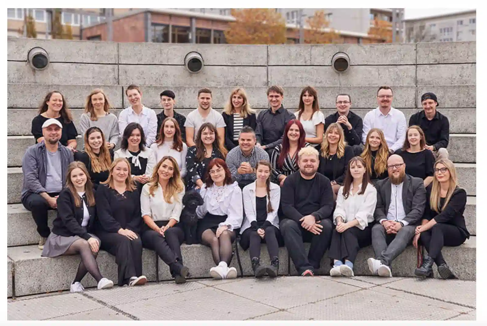 A large group of individuals sits on concrete steps, dressed in black and white attire, arranged in several rows outdoors.