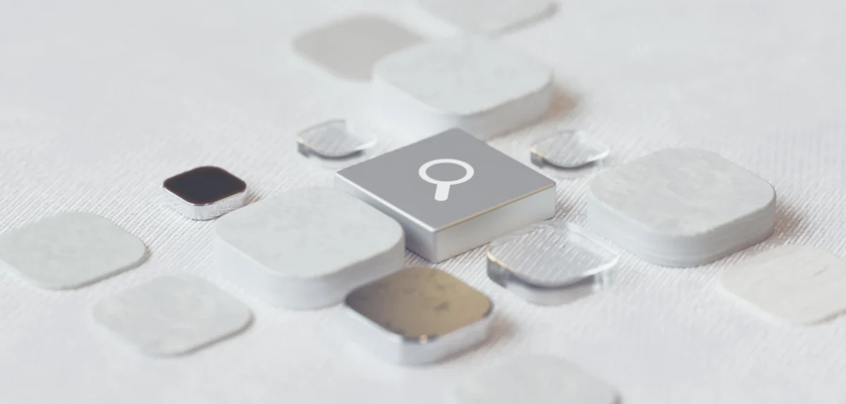 Close-up of scattered white and metallic square tiles with one tile featuring a magnifying glass icon on a textured white surface.