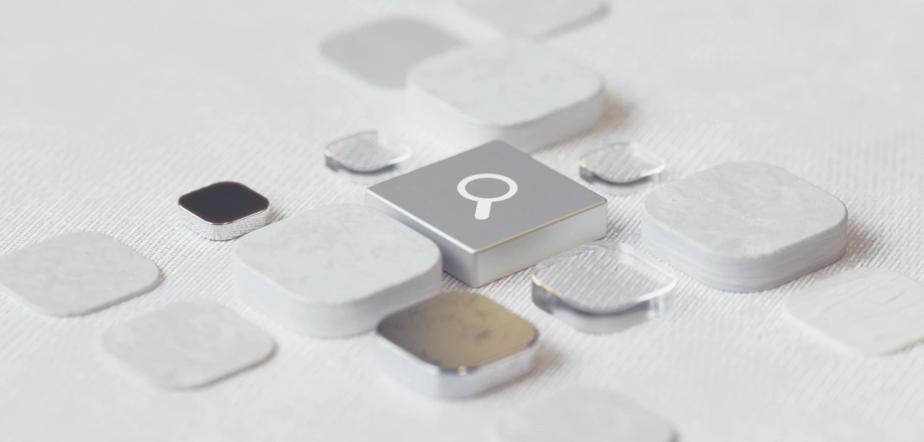 Close-up of scattered white and metallic square tiles with one tile featuring a magnifying glass icon on a textured white surface.