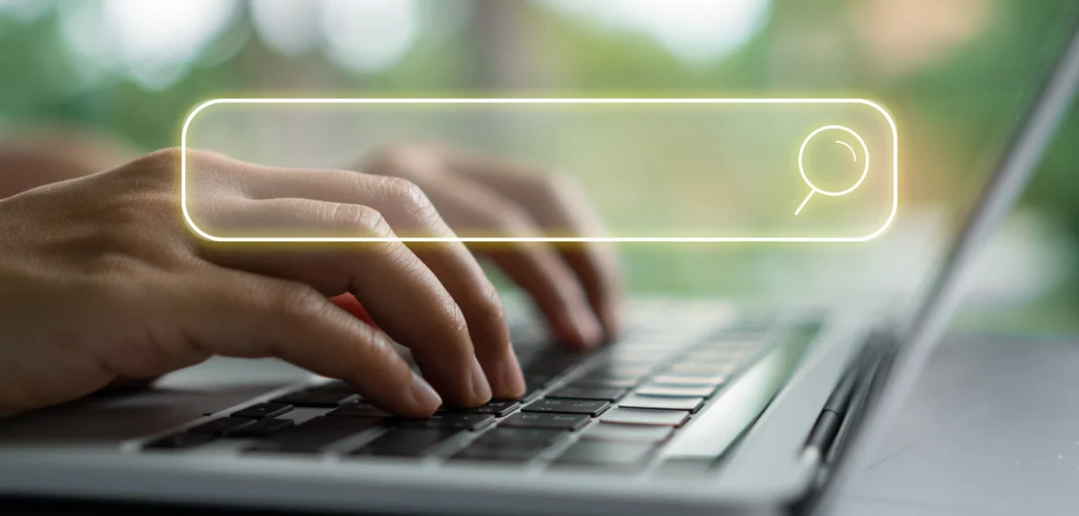 Hands typing on a laptop keyboard with a translucent search bar and magnifying glass icon overlay.