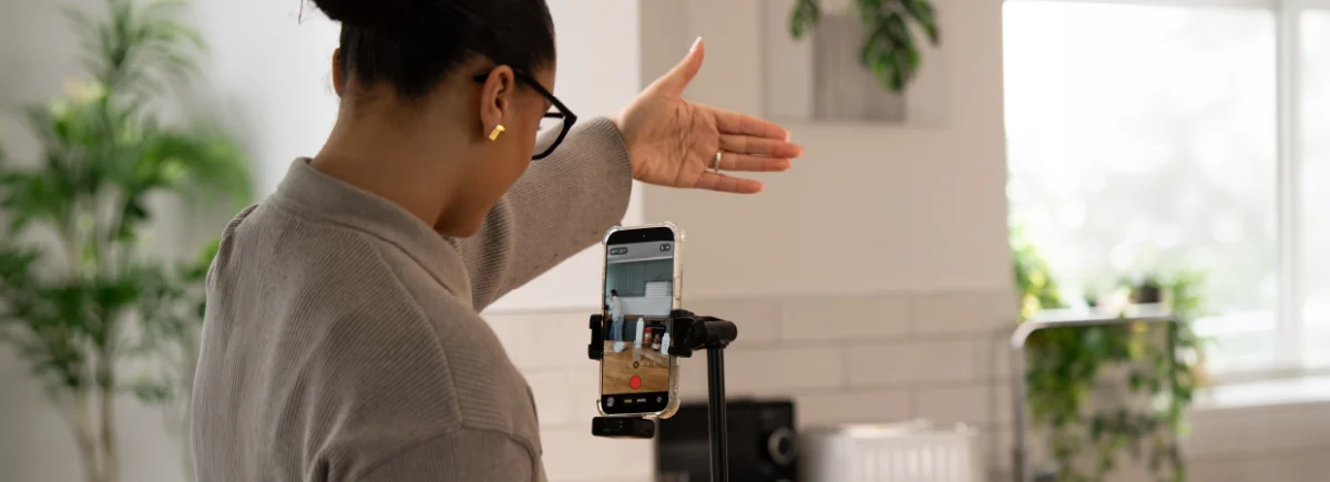 Person recording a video on a smartphone mounted on a tripod in a bright kitchen setting.