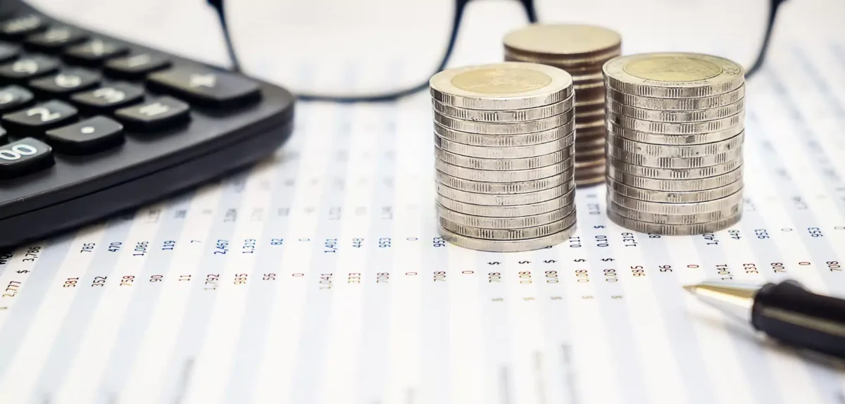 Stacks of coins, a calculator, and a pen on financial data sheets, symbolizing budgeting and accounting.