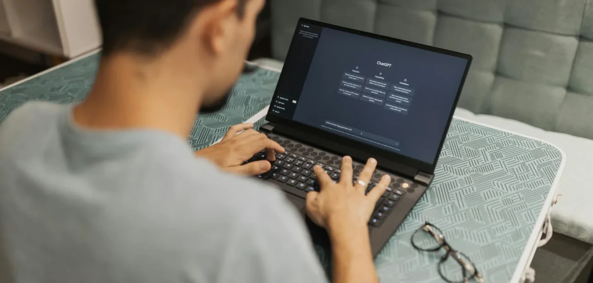 A man focused on typing on a laptop computer, seated at a desk in a well-lit room.