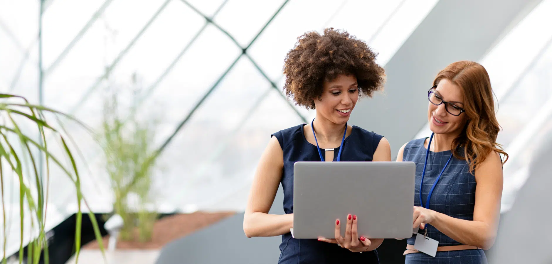 Two women in business attire collaborate while reviewing information on a laptop.