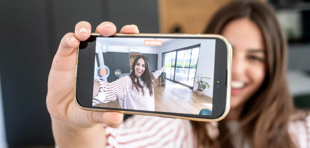 A woman smiling while holding a phone displaying a video chat with another person.