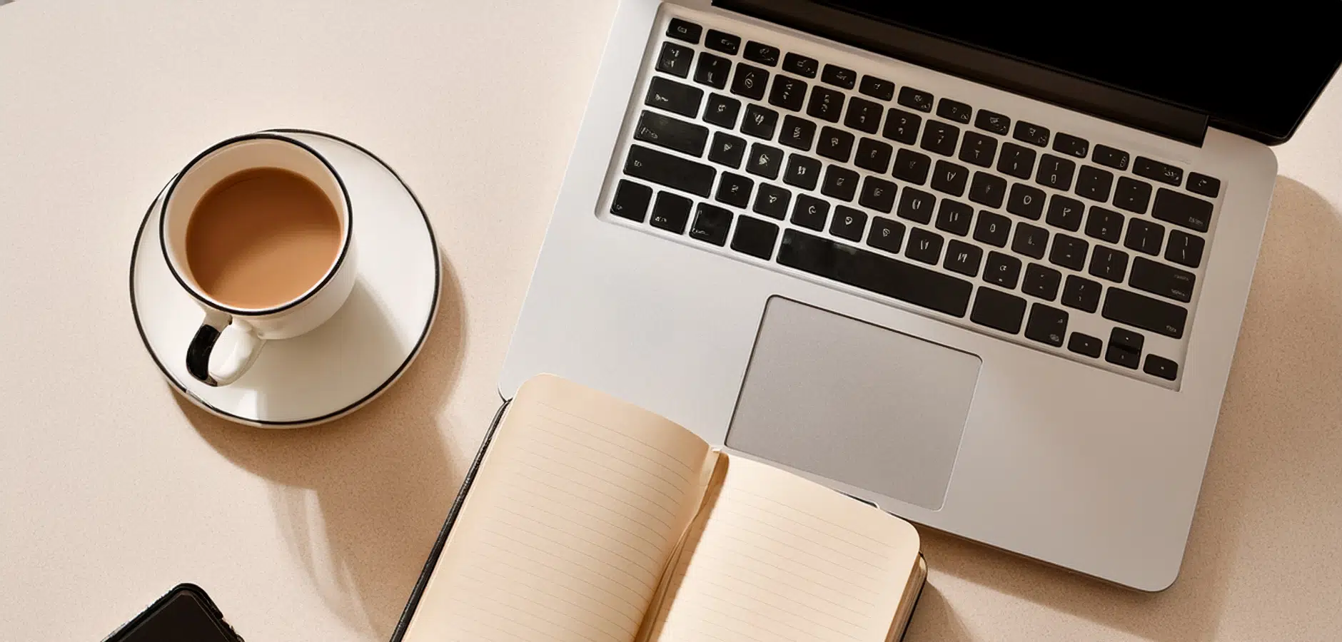 Top-down view of a laptop, open lined notebook, smartphone, and cup of coffee on a desk.